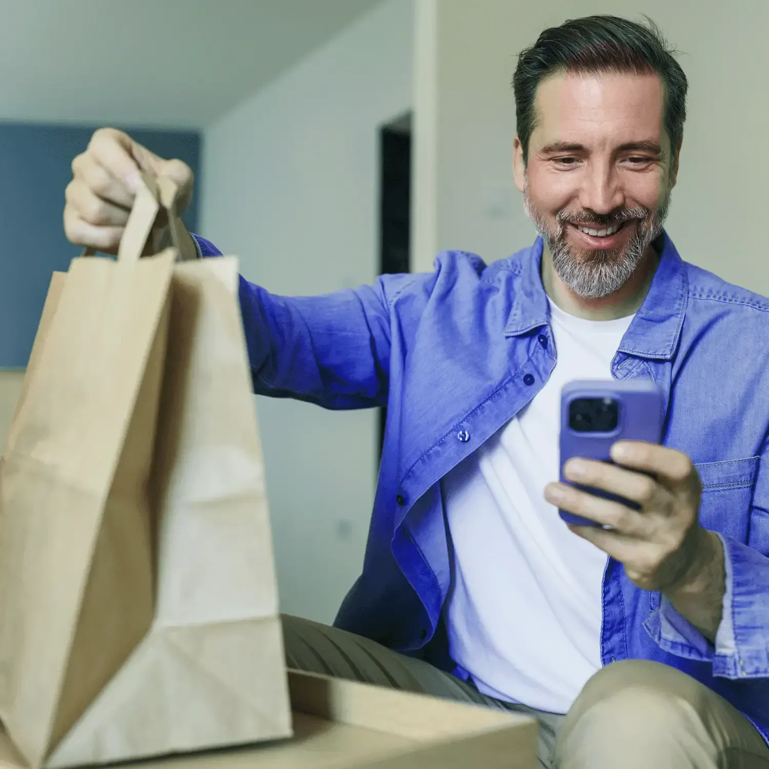 Homem sorridente segurando uma sacola de compras de papel enquanto mexe no celular.